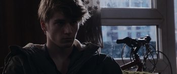 Movie still from “The Gentlemen” (2019), directed by Guy Ritchie – A young man in a jacket is looking at the camera; Close Up shot, Over the shoulder angle