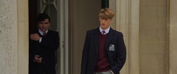 Movie still from “The Gentlemen” (2019), directed by Guy Ritchie – A man in a suit and tie standing in front of a building; Medium shot, Over the shoulder angle