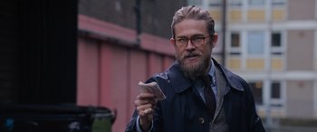 Movie still from “The Gentlemen” (2019), directed by Guy Ritchie – A man with a beard is holding money in his hand; Close Up shot, Over the shoulder angle
