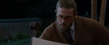 Movie still from “The Gentlemen” (2019), directed by Guy Ritchie – A man with a beard and glasses looking down at a piece of paper; Close Up shot, Over the shoulder angle
