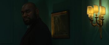 Movie still from “The Gentlemen” (2019), directed by Guy Ritchie – A man standing in front of a painting in a dark room; Medium shot, Low angle