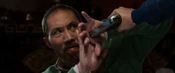 Movie still from “The Gentlemen” (2019), directed by Guy Ritchie – A man with a beard is holding a cell phone up to his mouth; Close Up shot, Overhead angle