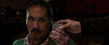 Movie still from “The Gentlemen” (2019), directed by Guy Ritchie – A man with a beard is holding a glass of alcohol; Close Up shot, Over the shoulder angle