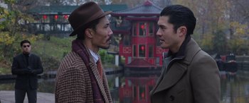 Movie still from “The Gentlemen” (2019), directed by Guy Ritchie – Two men standing next to each other in front of a building; Medium shot, Over the shoulder angle