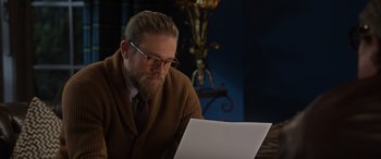 Movie still from “The Gentlemen” (2019), directed by Guy Ritchie – A man with a beard is looking at a paper; Medium shot, Over the shoulder angle