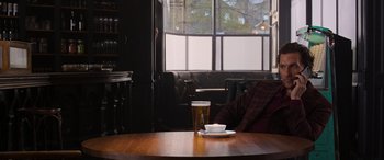 Movie still from “The Gentlemen” (2019), directed by Guy Ritchie – A person sitting at a table with a glass of beer; Medium shot, Over the shoulder angle