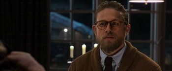 Movie still from “The Gentlemen” (2019), directed by Guy Ritchie – A person wearing glasses and a sweater; Close Up shot, Over the shoulder angle