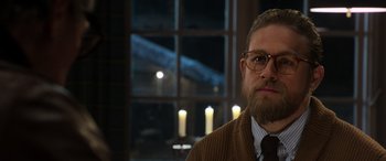 Movie still from “The Gentlemen” (2019), directed by Guy Ritchie – A man with a goatee and beard wearing glasses and a sweater; Close Up shot, Over the shoulder angle