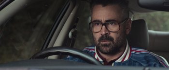Movie still from “The Gentlemen” (2019), directed by Guy Ritchie – A man with glasses is sitting in the driver's seat of a car; Close Up shot, Over the shoulder angle