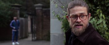 Movie still from “The Gentlemen” (2019), directed by Guy Ritchie – A person with a beard wearing glasses; Close Up shot, Over the shoulder angle
