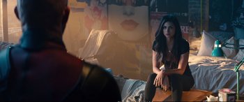Movie still from “Deadpool 2” (2018), directed by David Leitch – A woman sitting on top of a wooden table; Medium shot, Over the shoulder angle