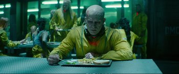 Movie still from “Deadpool 2” (2018), directed by David Leitch – A man in a yellow jacket is eating a sandwich; Medium shot, Over the shoulder angle