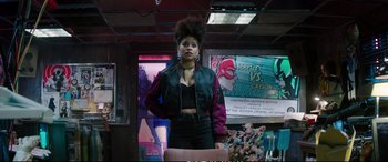 Movie still from “Deadpool 2” (2018), directed by David Leitch – A woman standing in front of a wall of posters; Medium shot, Over the shoulder angle