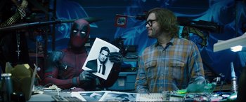 Movie still from “Deadpool 2” (2018), directed by David Leitch – A man holding up a picture of a man in a deadpool costume; Medium shot, Over the shoulder angle