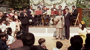 Movie still from “The Godfather” (1972), directed by Francis Ford Coppola – A group of men in suits and ties performing on stage; Medium shot, Low angle