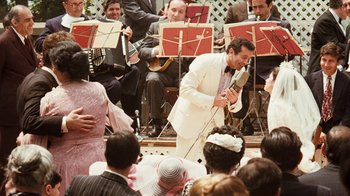Movie still from “The Godfather” (1972), directed by Francis Ford Coppola – A man in a white suit is holding a microphone; Wide shot, Over the shoulder angle