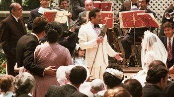 Movie still from “The Godfather” (1972), directed by Francis Ford Coppola – A man in a white suit is holding a microphone; Medium shot, Over the shoulder angle
