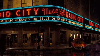 Movie still from “The Godfather” (1972), directed by Francis Ford Coppola – A neon sign is lit up on the side of a building; Wide shot, Low angle