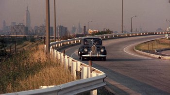 Movie still from “The Godfather” (1972), directed by Francis Ford Coppola – An old car is driving down the street; Extreme Wide shot, Over the shoulder angle