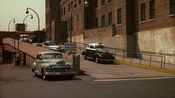 Movie still from “The Godfather” (1972), directed by Francis Ford Coppola – An old car is parked on the side of the road; Extreme Wide shot, High angle