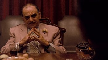 Movie still from “The Godfather” (1972), directed by Francis Ford Coppola – An older man sitting at a table with his hands crossed; Medium shot, Over the shoulder angle