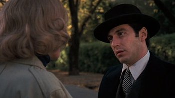 Movie still from “The Godfather” (1972), directed by Francis Ford Coppola – A man wearing a black hat talking to a woman wearing a black suit; Close Up shot, Over the shoulder angle