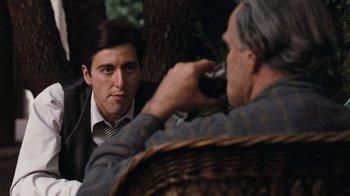 Movie still from “The Godfather” (1972), directed by Francis Ford Coppola – A man drinking a glass of red wine while looking at another man; Medium shot, Over the shoulder angle