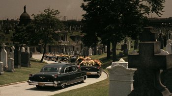 Movie still from “The Godfather” (1972), directed by Francis Ford Coppola – An old car is driving down the street with flowers on it; Extreme Wide shot, High angle