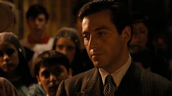 Movie still from “The Godfather” (1972), directed by Francis Ford Coppola – A man in a suit and tie with a bunch of people in the background; Close Up shot, Over the shoulder angle