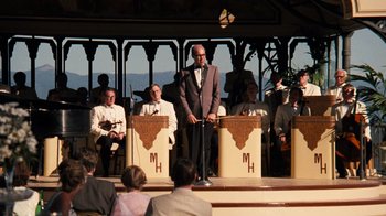 Movie still from “The Godfather Part II” (1974), directed by Francis Ford Coppola – A group of men standing on a stage with microphones; Wide shot, Over the shoulder angle
