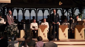Movie still from “The Godfather Part II” (1974), directed by Francis Ford Coppola – A man is speaking at an outdoor event; Medium shot, Over the shoulder angle