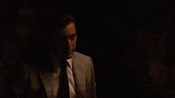 Movie still from “The Godfather Part II” (1974), directed by Francis Ford Coppola – A man wearing a suit and tie standing in the dark; Medium shot, Over the shoulder angle