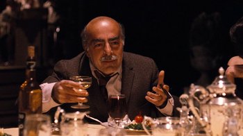 Movie still from “The Godfather Part II” (1974), directed by Francis Ford Coppola – An older man sitting at a table with a glass of wine; Medium shot, Over the shoulder angle