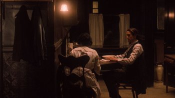 Movie still from “The Godfather Part II” (1974), directed by Francis Ford Coppola – Two people sitting at a table in a dimly - lit room; Medium shot, High angle