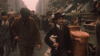 Movie still from “The Godfather Part II” (1974), directed by Francis Ford Coppola – A man in a suit and hat walking down a street; Medium shot, High angle