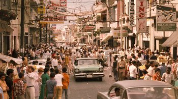 Movie still from “The Godfather Part II” (1974), directed by Francis Ford Coppola – A crowd of people walking down a street next to a car; Extreme Wide shot, High angle