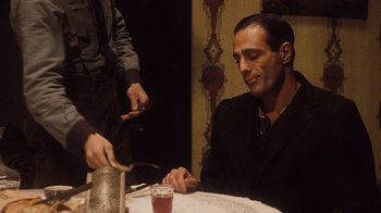Movie still from “The Godfather Part II” (1974), directed by Francis Ford Coppola – A man sitting at a table with a drink in front of him; Medium shot, Over the shoulder angle