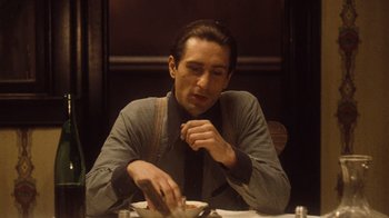Movie still from “The Godfather Part II” (1974), directed by Francis Ford Coppola – A man sitting at a table eating a meal; Medium shot, Low angle