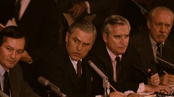 Movie still from “The Godfather Part II” (1974), directed by Francis Ford Coppola – Two men in suits and ties sitting at microphones in front of microphones; Close Up shot, Over the shoulder angle