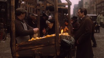 Movie still from “The Godfather Part II” (1974), directed by Francis Ford Coppola – An old fashioned fruit stand with people looking at it; Medium shot, High angle