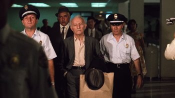 Movie still from “The Godfather Part II” (1974), directed by Francis Ford Coppola – An older man in a suit and tie is surrounded by police; Medium shot, Over the shoulder angle