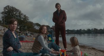 Movie still from “The Good House” (2021), directed by Maya Forbes – Two people and a child sitting on the beach near the water; Medium shot, Over the shoulder angle