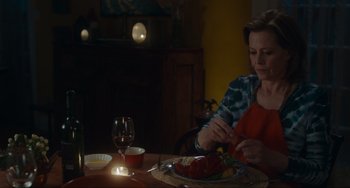 Movie still from “The Good House” (2021), directed by Maya Forbes – A woman sitting at a table with a plate of food in front of her; Medium shot, Over the shoulder angle
