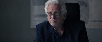 Movie still from “The Good Neighbor” (2022), directed by Stephan Rick – An older man with white hair wearing a suit; Close Up shot, Over the shoulder angle