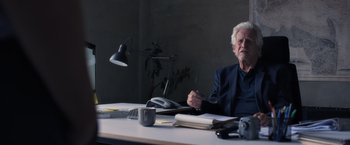 Movie still from “The Good Neighbor” (2022), directed by Stephan Rick – An older man sitting at a desk in front of a lamp; Medium shot, Over the shoulder angle
