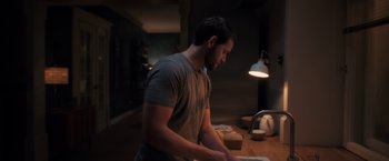 Movie still from “The Good Neighbor” (2022), directed by Stephan Rick – A man standing at a table in front of a lamp; Medium shot, Low angle