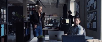 Movie still from “The Good Neighbor” (2022), directed by Stephan Rick – A woman standing in front of a laptop computer in an office; Wide shot, Over the shoulder angle