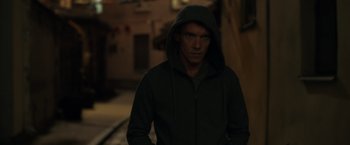 Movie still from “The Good Neighbor” (2022), directed by Stephan Rick – A man wearing a hooded jacket standing in a dark room; Close Up shot, Low angle