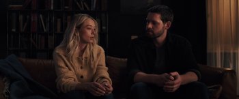 Movie still from “The Good Neighbor” (2022), directed by Stephan Rick – A man and a woman sitting next to each other on a couch; Medium shot, Over the shoulder angle