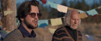 Movie still from “The Good Neighbor” (2022), directed by Stephan Rick – A man with a beard and sunglasses is next to another man; Close Up shot, Low angle